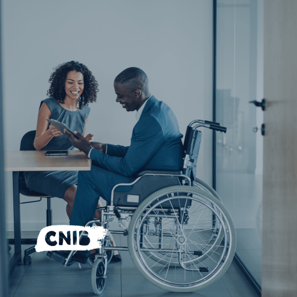 A woman is seated at a table showing a clipboard to a man in a wheelchair